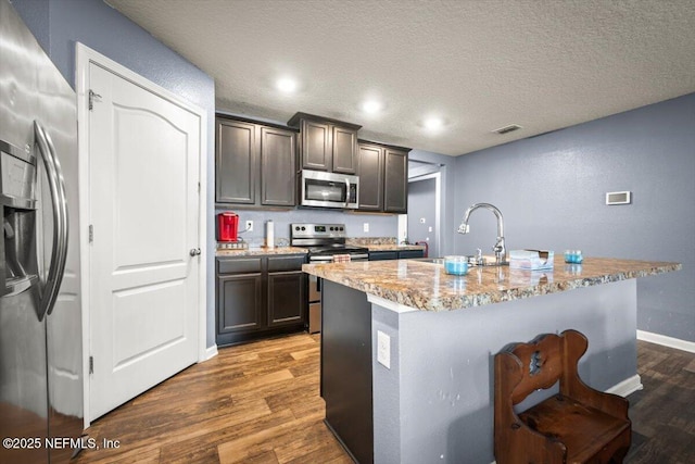 kitchen with sink, a kitchen island with sink, stainless steel appliances, dark wood-type flooring, and a textured ceiling