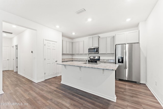 kitchen featuring appliances with stainless steel finishes, a kitchen island with sink, dark wood-type flooring, and light stone counters