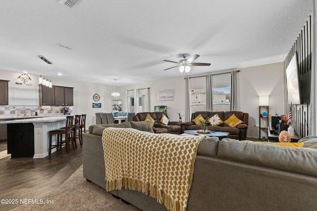 living room featuring ceiling fan with notable chandelier, a textured ceiling, and dark hardwood / wood-style flooring