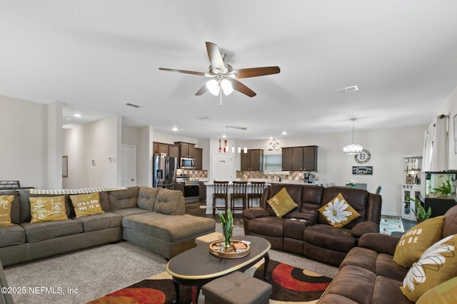 carpeted living room featuring ceiling fan with notable chandelier