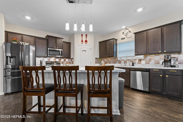 kitchen with hanging light fixtures, backsplash, stainless steel appliances, a center island, and dark brown cabinetry