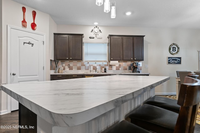 kitchen with a center island, dark brown cabinets, dark hardwood / wood-style flooring, pendant lighting, and decorative backsplash