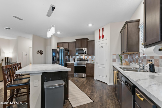 kitchen featuring a breakfast bar area, appliances with stainless steel finishes, hanging light fixtures, dark hardwood / wood-style floors, and a center island