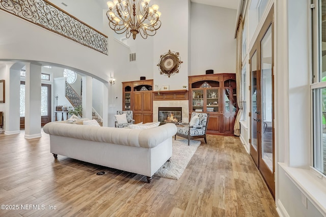 living room with a tiled fireplace, an inviting chandelier, light wood-type flooring, and ornate columns