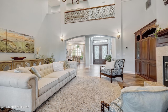 living room with hardwood / wood-style flooring, a towering ceiling, and a high end fireplace