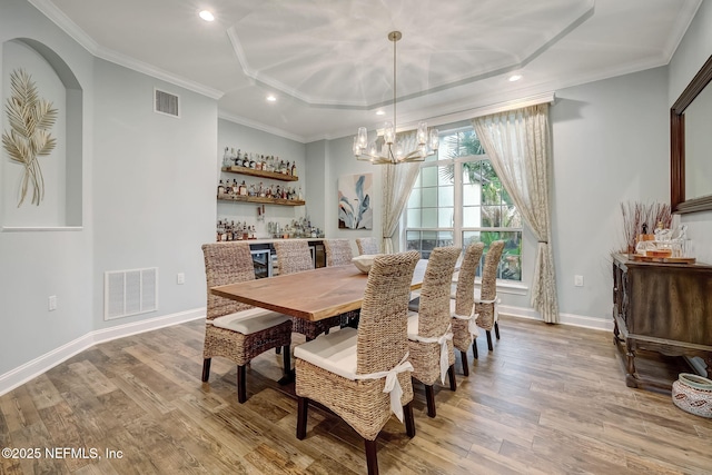 dining room with an inviting chandelier, ornamental molding, wood-type flooring, and bar