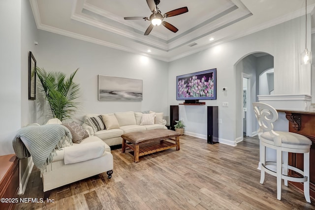 living room featuring a raised ceiling, crown molding, hardwood / wood-style flooring, and ceiling fan