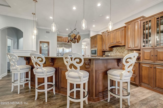 kitchen with a breakfast bar area, built in appliances, hanging light fixtures, a kitchen island, and decorative backsplash