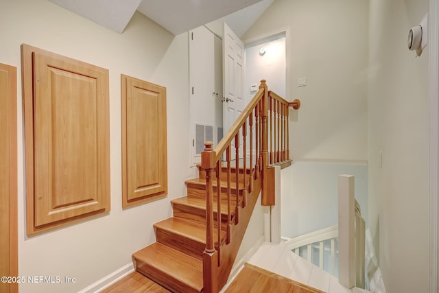 stairs featuring wood-type flooring and vaulted ceiling