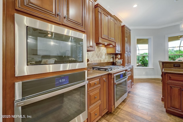 kitchen featuring crown molding, appliances with stainless steel finishes, light wood-type flooring, and decorative backsplash