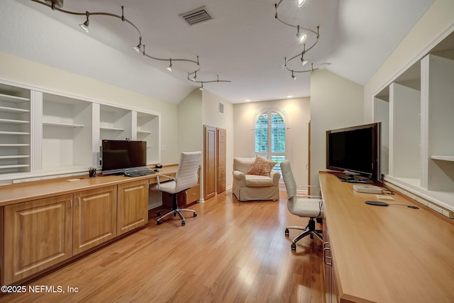 office space with vaulted ceiling, rail lighting, light hardwood / wood-style floors, and built in shelves