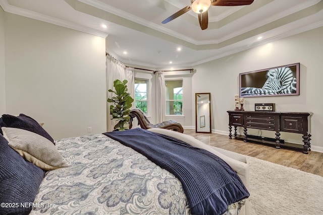 bedroom featuring ceiling fan, ornamental molding, a tray ceiling, and light hardwood / wood-style floors