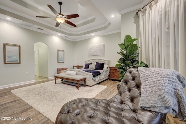 bedroom with ceiling fan, ornamental molding, a tray ceiling, and light hardwood / wood-style flooring