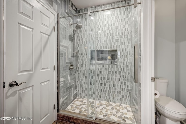 bathroom featuring a shower with door and toilet