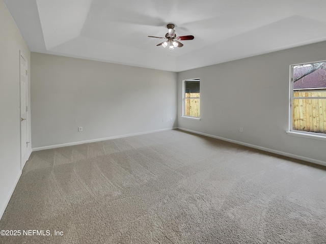 carpeted spare room with a raised ceiling and ceiling fan