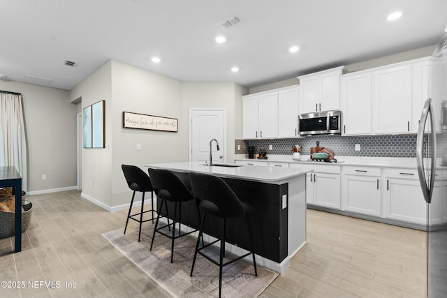 kitchen featuring sink, an island with sink, decorative backsplash, and white cabinets