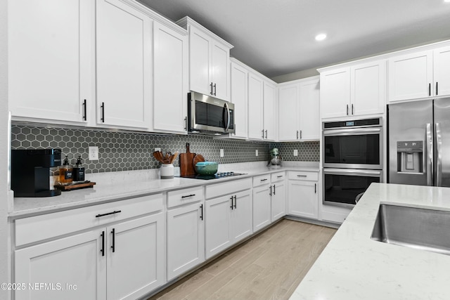 kitchen with white cabinetry, decorative backsplash, light stone counters, stainless steel appliances, and light wood-type flooring