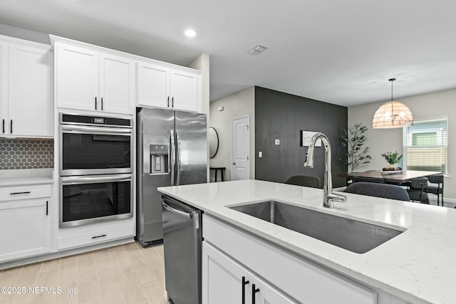 kitchen featuring stainless steel appliances, sink, white cabinets, and decorative light fixtures