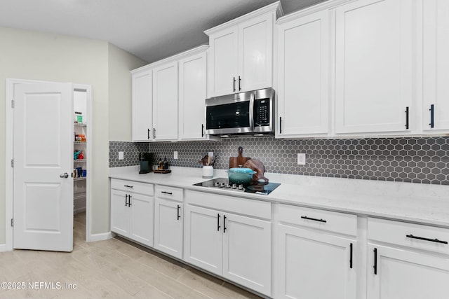 kitchen featuring tasteful backsplash, white cabinetry, black electric stovetop, light stone counters, and light hardwood / wood-style flooring