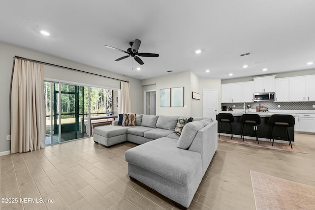 living room with ceiling fan, sink, and light wood-type flooring