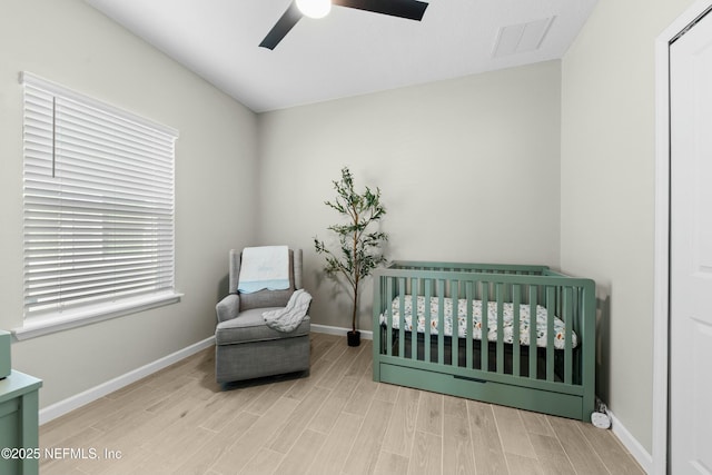 bedroom with a crib, ceiling fan, and light wood-type flooring