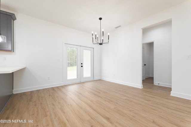 unfurnished dining area featuring a chandelier, light hardwood / wood-style floors, and french doors