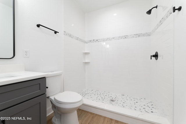 bathroom with wood-type flooring, a tile shower, vanity, and toilet