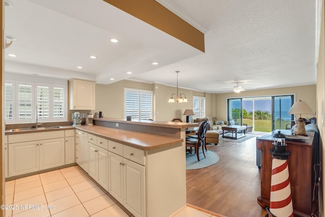 kitchen with sink, light hardwood / wood-style flooring, a textured ceiling, kitchen peninsula, and pendant lighting