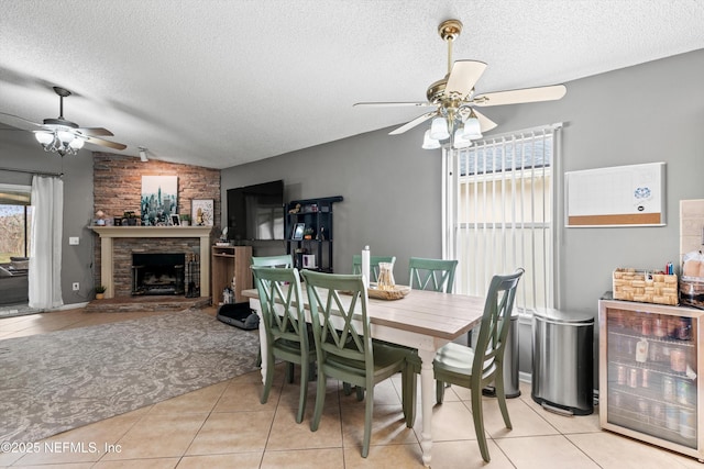 tiled dining room with vaulted ceiling, a textured ceiling, beverage cooler, ceiling fan, and a fireplace