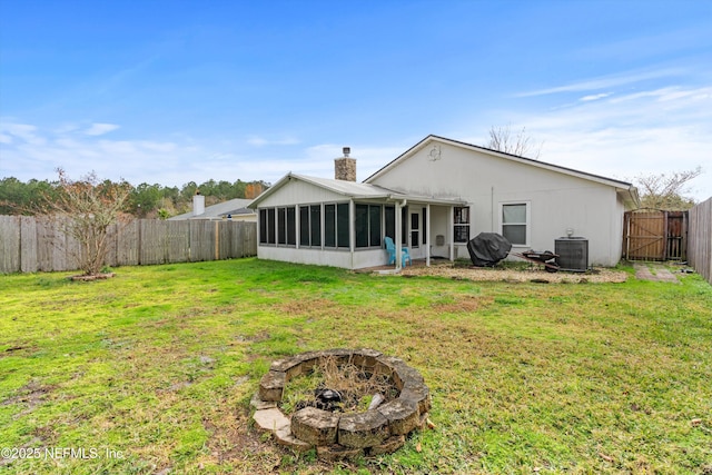 back of property with a sunroom, a yard, central AC, and an outdoor fire pit