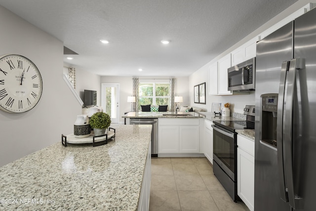 kitchen featuring sink, light tile patterned floors, appliances with stainless steel finishes, white cabinetry, and light stone counters