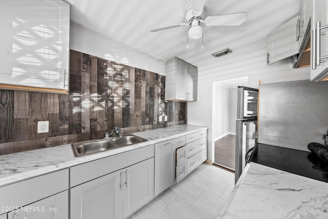 kitchen with gray cabinets, light stone countertops, sink, and stainless steel fridge