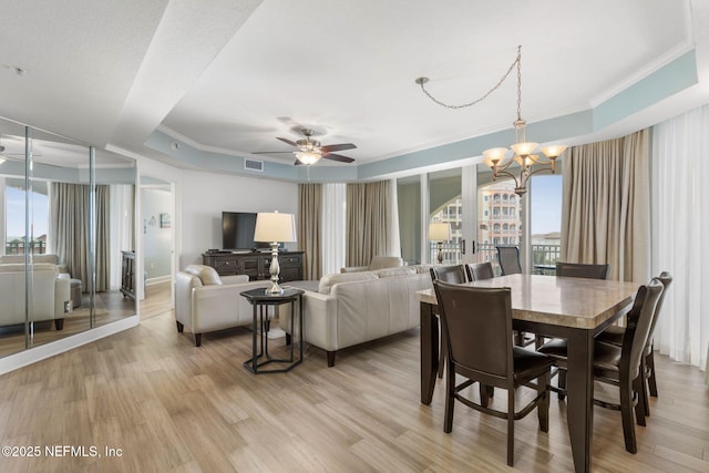 dining area featuring crown molding, ceiling fan with notable chandelier, light wood-type flooring, and a tray ceiling