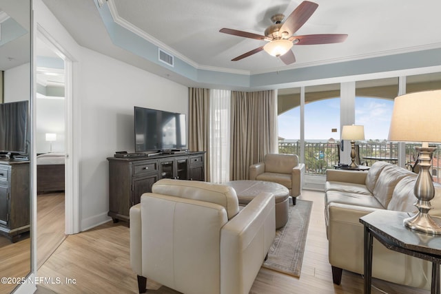 living room with a tray ceiling, light hardwood / wood-style flooring, ornamental molding, and ceiling fan