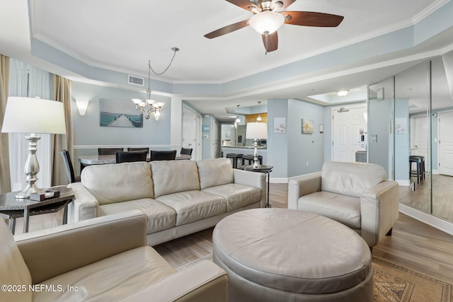 living room with a raised ceiling, crown molding, ceiling fan with notable chandelier, and light wood-type flooring