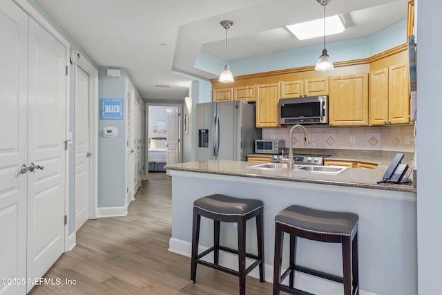 kitchen with appliances with stainless steel finishes, sink, light brown cabinetry, and kitchen peninsula