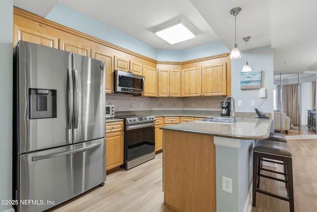 kitchen featuring sink, a breakfast bar area, kitchen peninsula, stainless steel appliances, and light brown cabinets