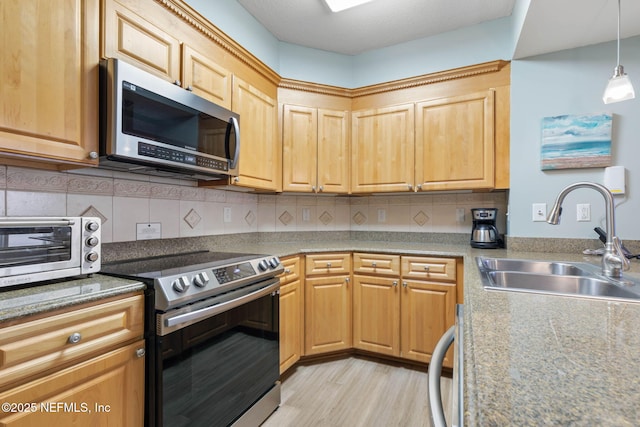 kitchen with tasteful backsplash, sink, hanging light fixtures, stainless steel appliances, and light hardwood / wood-style flooring