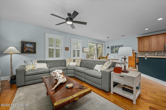 living room with ceiling fan, a wealth of natural light, light hardwood / wood-style flooring, and a textured ceiling