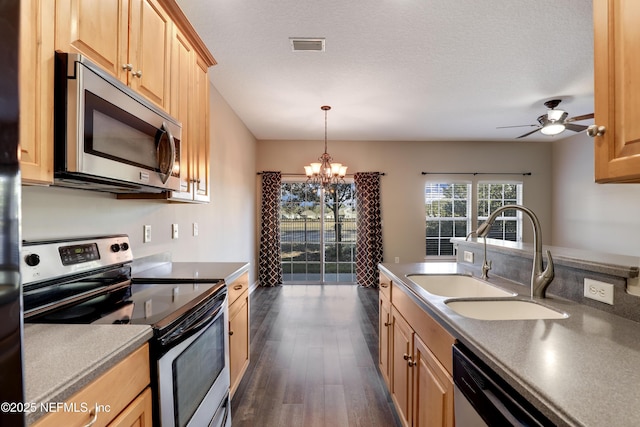 kitchen with pendant lighting, sink, dark wood-type flooring, stainless steel appliances, and ceiling fan with notable chandelier