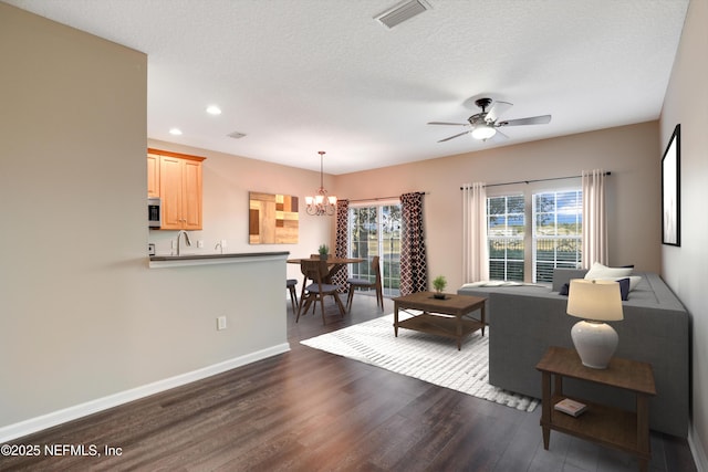 living room with sink, dark hardwood / wood-style floors, ceiling fan with notable chandelier, and a textured ceiling