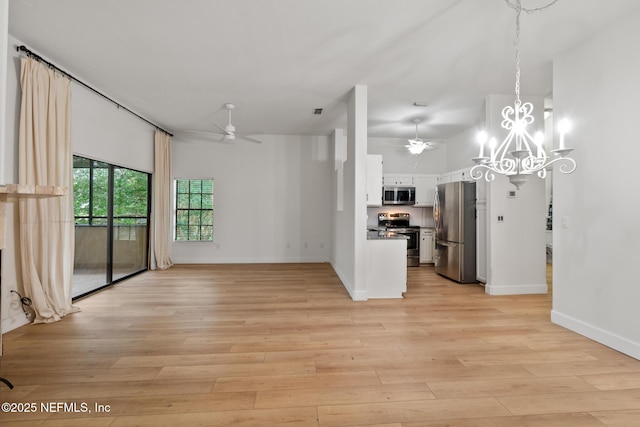 unfurnished living room with ceiling fan with notable chandelier, a high ceiling, and light wood-type flooring