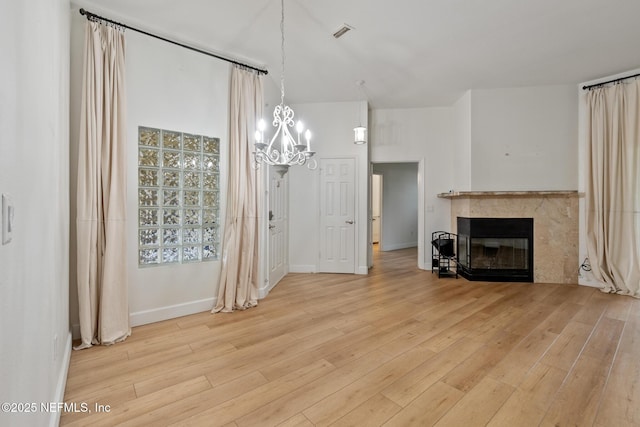 unfurnished living room featuring light hardwood / wood-style floors, a high ceiling, and a notable chandelier