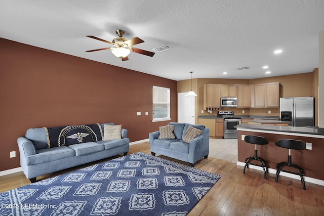 living room with a textured ceiling, ceiling fan, and light hardwood / wood-style flooring