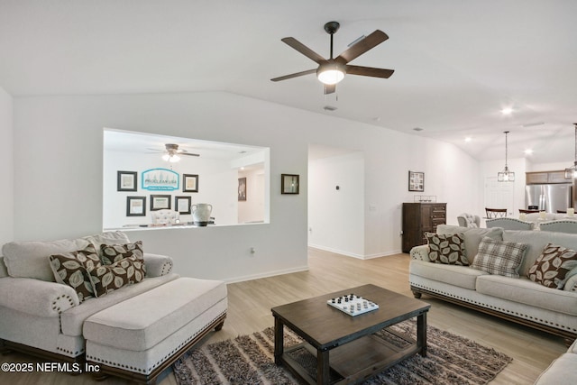 living room featuring vaulted ceiling, ceiling fan with notable chandelier, and light wood-type flooring