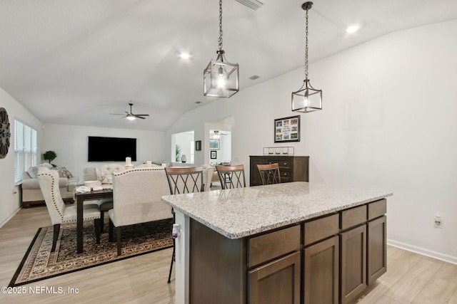 kitchen featuring light stone counters, a kitchen island, hanging light fixtures, and light wood-type flooring