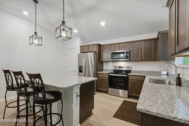 kitchen with a kitchen island, appliances with stainless steel finishes, pendant lighting, sink, and light stone countertops