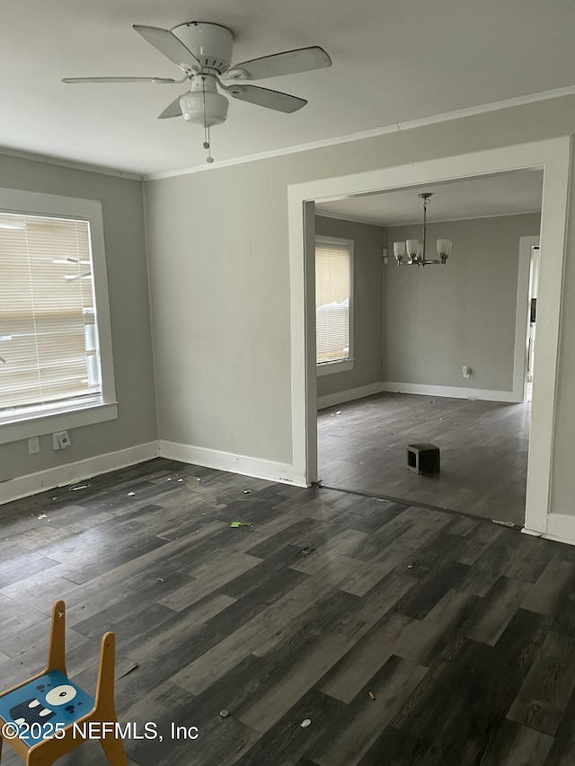 empty room featuring dark wood-type flooring, ornamental molding, and ceiling fan with notable chandelier