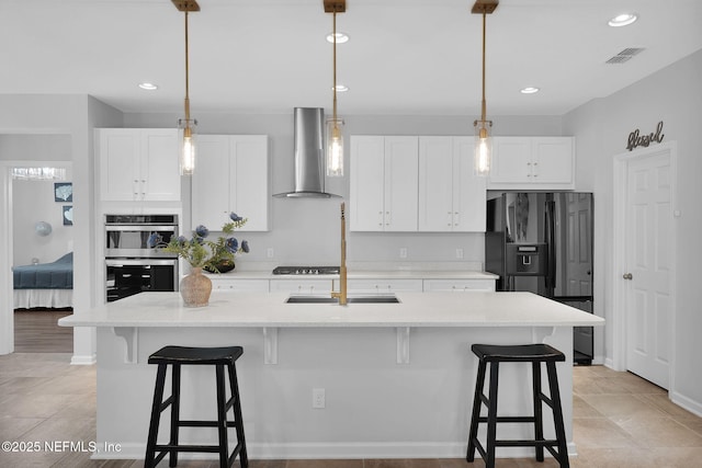 kitchen with a kitchen island with sink, wall chimney range hood, white cabinetry, and stainless steel appliances