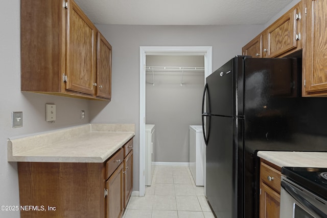 kitchen with black refrigerator, light tile patterned floors, a textured ceiling, and washing machine and clothes dryer